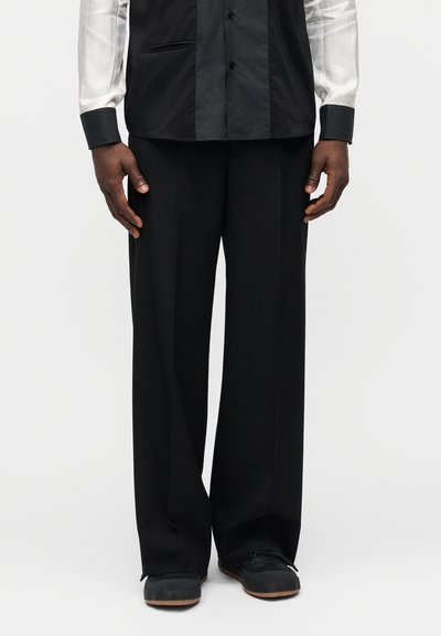 Black wide-leg trousers made of smooth fabric, featuring a relaxed fit and accented with concealed side pockets and a sleek waistband.