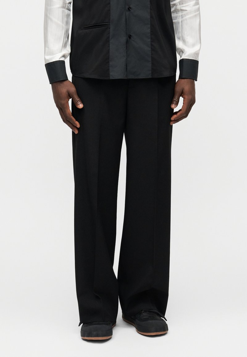 Pantalon noir à jambes larges en tissu lisse, caractérisé par une coupe décontractée et agrémenté de poches latérales dissimulées ainsi que d'une ceinture élégante.