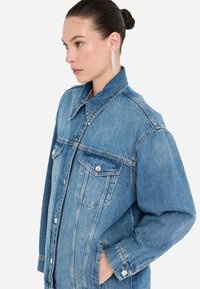 La giacca di jeans presenta un colore blu chiaro, maniche lunghe, un grande colletto, tasche anteriori e bottoni metallici, con una vestibilità comoda e una texture morbida.