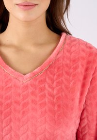 Sudadera de forro polar de coral con cuello en V, presenta un patrón texturizado en zigzag y un acento dorado a lo largo del escote. Material suave y acogedor.