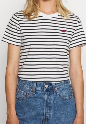 Femme portant un t-shirt Levi’s rayé blanc et noir, rentré dans un jean en denim bleu taille haute, visible du cou aux hanches.