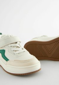 Hvide sneakers med grønne accenter, der har en glat overflade, justerbar rem og mønstret gummisål for greb og stabilitet.