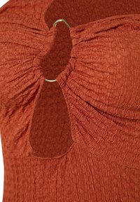 Robe rouille froncée avec une découpe en œillet au niveau du décolleté, accentuée par un anneau doré. Tissu texturé avec un léger éclat.