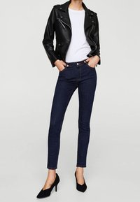 Musta nahkainen moottoripyöräilijän takki, valkoinen t-paita, tummansiniset kapeat farkut ja mustat korkokengät. Yksinkertainen, vartalonmyötäinen malli ja sileä pinta.