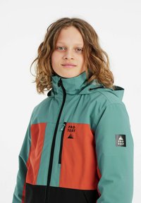 Giacca outdoor colorata con una parte superiore blu teal, una parte centrale arancione e una parte inferiore nera; presenta una cerniera, cappuccio e dettagli con logo.