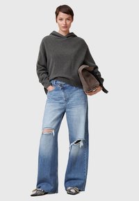 Grå huvad tröja, löst sittande ljusblå jeans med slitna knän och svarta texturerade loafers, kombinerat med en mörk handväska.