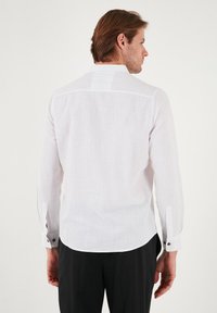 Camisa blanca de manga larga hecha de lino texturizado, con un cuello clásico, puños abotonados y un dobladillo recto. Diseño minimalista con detalles sutiles.