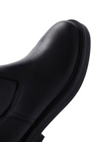 Zwarte leren enkelboot met een ronde neus, een gladde textuur, minimale stiksels en een dikke, gestructureerde rubberen zool.