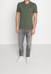 Polo vert avec col, deux boutons et logo brodé. Associé à un jean gris clair et des baskets blanches. Texture en coton lisse.