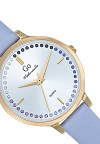 Montre en quartz dorée avec un cadran argenté en éclat de soleil, des accents de cristaux bleus et violets, et un bracelet en cuir bleu clair.