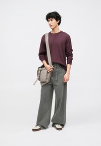 Bordowa koszula z długim rękawem, szare dżinsy o szerokich nogawkach oraz beżowa torebka na ramię. Buty w kolorze ecru z brązowymi akcentami. Całość o prostym designie.