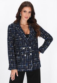 Sininen kaksirivinen blazer, jossa on teksturoitu kudottu kuvio, jossa on sinisiä, valkoisia ja keltaisia yksityiskohtia; suuret napit; ja lovetut kaulukset.