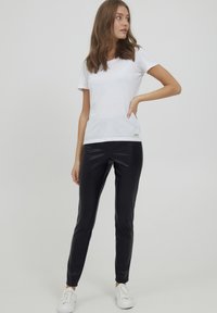 Witte t-shirt met korte mouwen gecombineerd met zwarte leren fitted broek en witte sneakers; gladde stof, minimalistisch ontwerp, casual uitstraling.