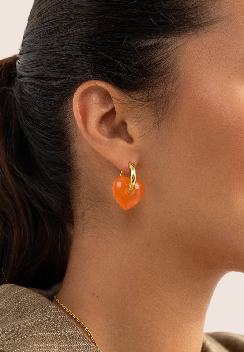 Orecchini a forma di cuore realizzati in resina arancione con un accento in oro. Il design è lucido, con una texture liscia e un colore vivace.