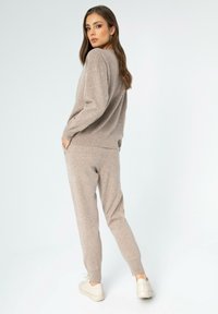 Beige Strickpullover und passende Jogginghosen, beide mit einer weichen Textur, lockerer Passform und gerippten Bündchen, kombiniert mit weißen Sneakers.