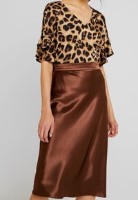 Haut en imprimé léopard avec des manches volantées, associé à une jupe midi en satin marron. Le haut a un décolleté en V ; la jupe a une finition lisse.