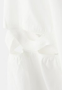 Material alb cu benzi texturate și detalii mici decupate de-a lungul unei cusături, prezentând secțiuni de țesătură stratificate și adunate.