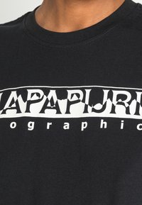 Sort bomulds t-shirt med et stort hvidt grafisk print med teksten "NAPAPIJRI" og stiliserede accenter på tværs af brystet.