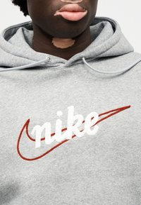Γκρι φούτερ με κουκούλα κατασκευασμένο από απαλό ύφασμα, με κεντητό λευκό λογότυπο "nike" και κόκκινη διακριτική γραμμή. Διαθέτει κουκούλα με κορδόνια και ριμπ μανσέτες.
