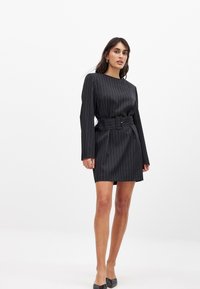Robe noire à rayures avec manches longues, encolure ronde et taille ceinturée. Tissu lisse avec une coupe légèrement structurée.