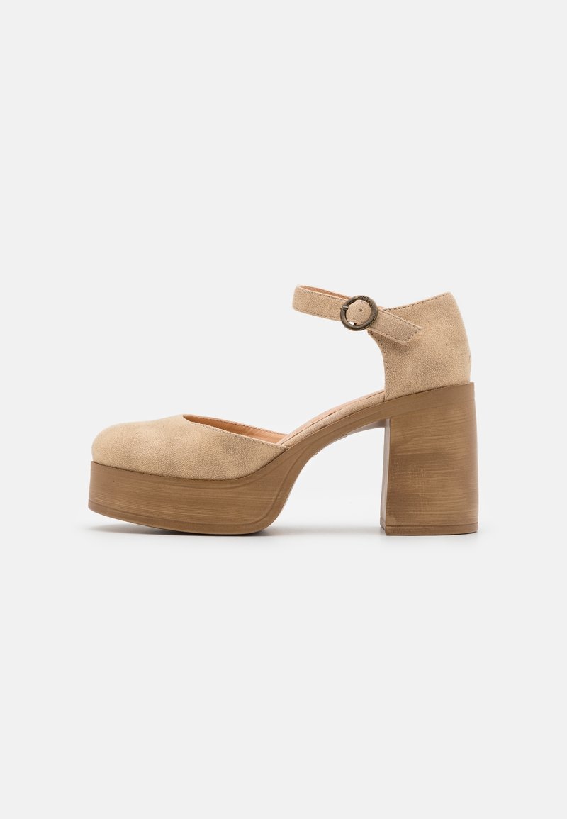 Chaussure plateforme en daim beige avec un talon bloc épais en bois et une bride de cheville avec une boucle ronde.