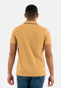 Polo shirt en jaune moutarde, manches courtes, en mélange de coton doux, avec des finitions noires au col, ourlet droit, porté avec un jean en denim bleu.