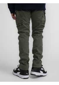 Olijfgroene cargobroek met zijzakken, taps toelopende pijpen en een gestructureerde stof. Gecombineerd met zwart-witte sneakers.