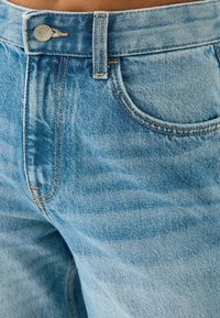 Ljusblå denimjeans med knappstängning, bältesslingor och detaljerade framfickor. Tyget har en något urtvättad struktur.