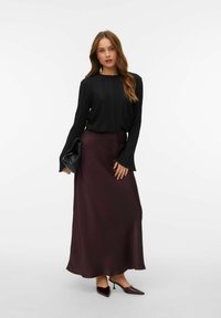 Sort ribbet langærmet top, der er parret med en mørk burgunderrød satin maxi-nederdel. Modellen holder en sort clutch og bærer spidse mørke hæle.