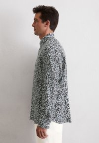 Langärmliges Hemd aus leichtem Stoff mit einem dunklen Blumenmuster in Grautönen, Blau und Grün; Button-Down-Kragen; lockere Passform.