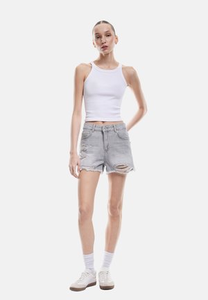 Shorts en denim gris avec des bords effilochés et des détails usés, assortis à un débardeur blanc à côtes et à des baskets blanches avec des accents gris.