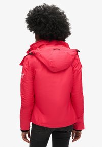 Czerwona ocieplana kurtka z kapturem, posiadająca taliowanie, kieszenie na zamek oraz fakturowaną tkaninę. Widok od tyłu ukazuje detale projektu.