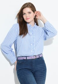 Camicia a righe blu e bianche con colletto arricciato, abbinata a jeans blu scuro e una cintura lavanda. Tessuto morbido e stile aderente.