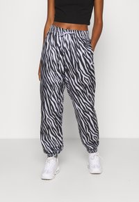 Kalhoty na jogging s zebřími pruhy v černé a bílé barvě, s elastickým pasem, bočními kapsami a zúženými manžetami. Vyrobeno z lehkého materiálu.