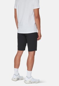 Svarta shorts med en avslappnad passform, tillverkade av ett lätt material, i kombination med en vit t-shirt och ljusgrå träningsskor.