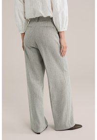 Világosszürke, széles szárú nadrág strukturált anyagból, enyhe mintával és magas derékkal, sötétbarna hegyes orrú cipővel párosítva.