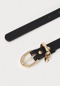Cinturón de cuero negro con hebilla de metal dorado, charm de corazón y agujeros ajustables. Textura suave, diseño elegante y estilo minimalista.