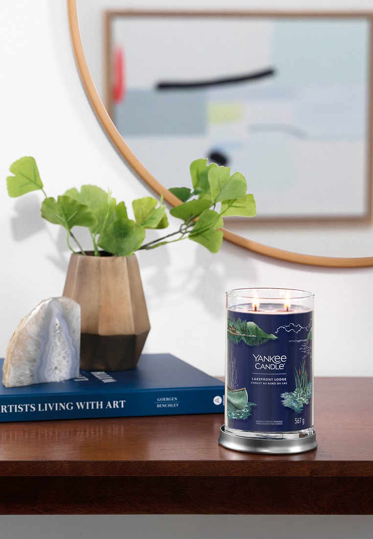 Świeca Yankee Candle w przezroczystym szklanym słoiku z metalową, srebrną podstawą, z designem przedstawiającym brzeg jeziora w odcieniach niebieskiego i zielonego, zapalona dwoma płomieniami.
