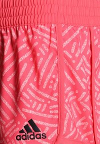 Pantalones cortos deportivos rosas de tela ligera, con un patrón blanco texturizado y el logo negro de Adidas en la parte frontal izquierda.