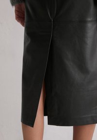 Czarna skórzana spódnica o długości do kolan, z bocznym rozcięciem, gładką fakturą i schludnymi szwami. Widoczny dół przy hemie.