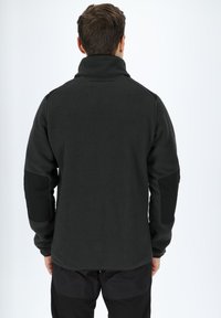 Giacca in pile grigia scura, con colletto alto, toppe nere sui gomiti e una superficie testurizzata. Design semplice e funzionale.
