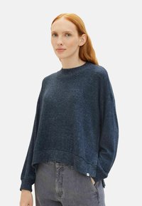 Pulover bleumarin cu finisaj texturat, guler rotund și croială oversized. Are mâneci lungi și un tiv ușor scurt.