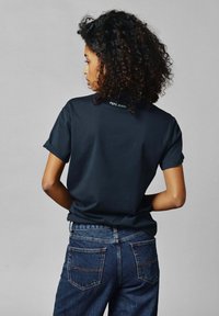 Zwarte katoenen t-shirt met opgerolde mouwen, met het "PEPE JEANS" logo op de achterkant van de hals. Gepaard met hoog-waisted blauwe spijkerbroek.