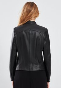 Black leather jacket featuring a tailored cut, smooth texture, and structured seams. Collar with button accents on sleeves.