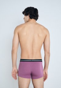 Purple men's boxer briefs with a black and silver waistband, featuring a snug fit and smooth texture. Back view, model facing away.