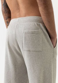 Grijze katoenen joggers met een gestructureerde afwerking, voorzien van een achterzak en een elastische tailleband. De stof lijkt zacht en ademend.