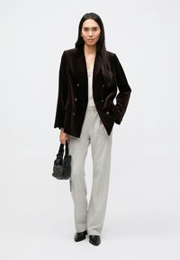 Sötétbarna dupla soros bársony blézer világos felsővel, szürke nadrággal és texturált fekete kézitáskával párosítva. Fekete hegyes végű cipők.