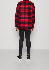 Camicia di flanella a quadri rossi e neri con maniche lunghe, abbinata a jeans skinny scuri e sneakers nere con suola e logo bianco.
