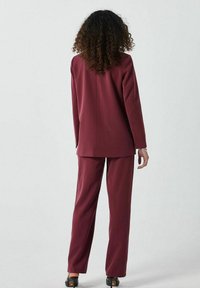 Costume bordeaux en deux pièces avec un blazer ajusté et un pantalon droit. Texture lisse, coutures minimales et détails de surpiqûres discrets.