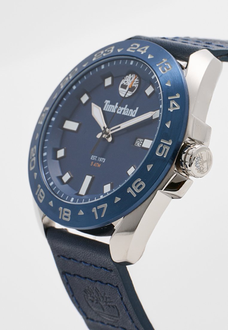 Reloj Timberland con esfera azul, caja de acero inoxidable plateado, correa de cuero azul marino, marcadores de hora blancos y un indicador de fecha a las 3 en punto.